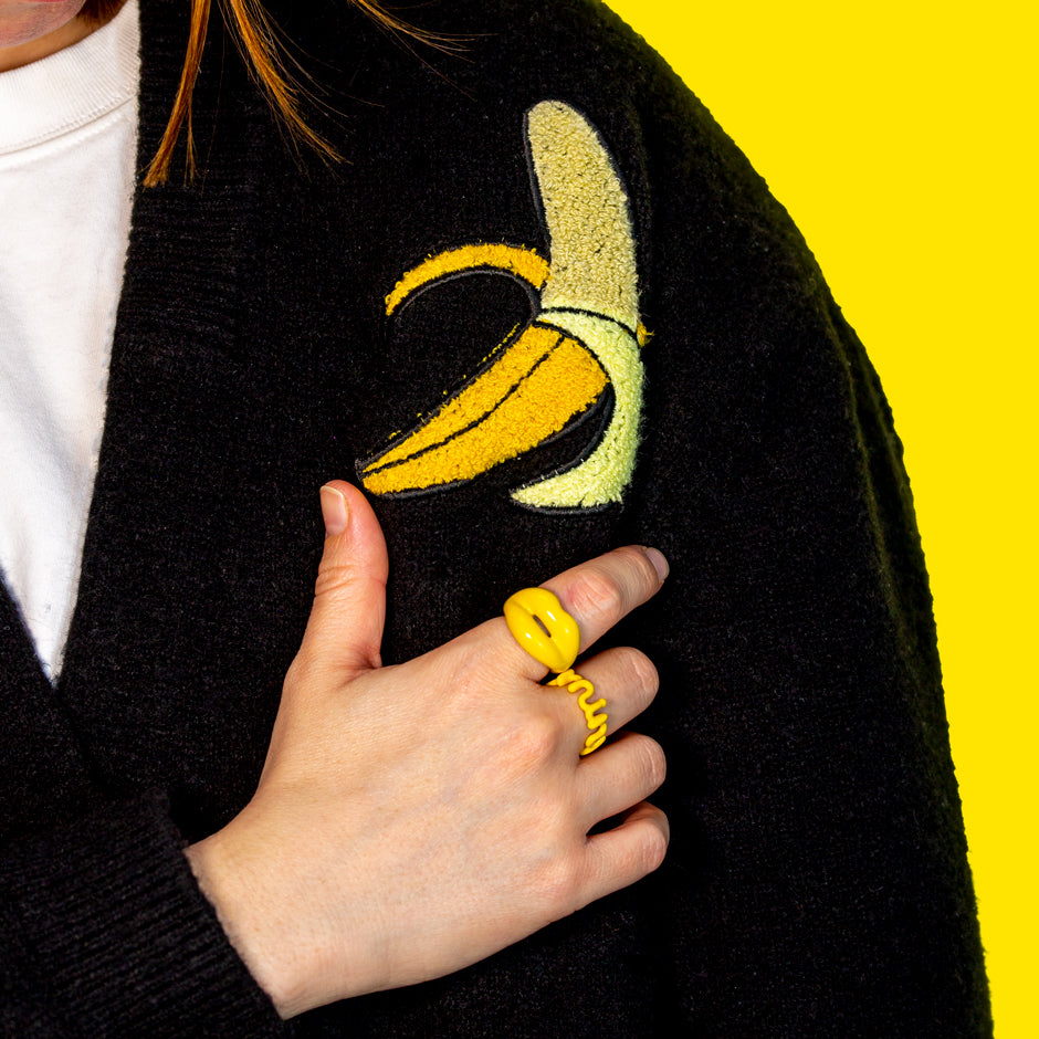Banana Yellow Hotlips ring and Minx ring on hand next to a banana applique sweater